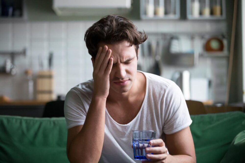 A man suffering with a headache while holding a glass of water.