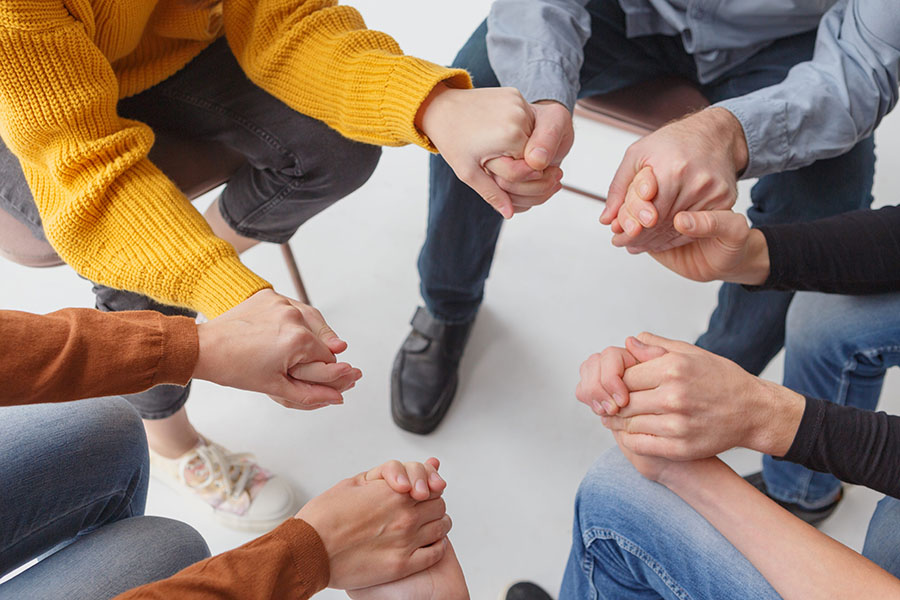 Group therapy participants hold hands during a session. 
