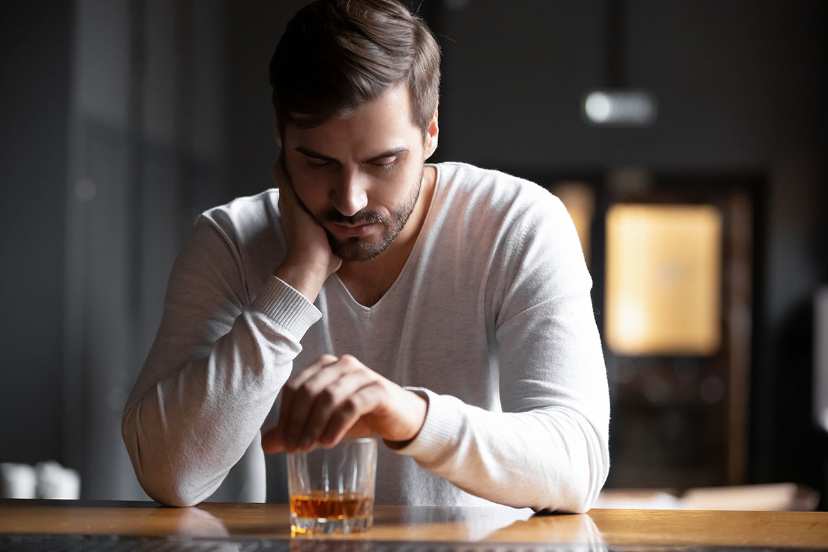 An upset man looking at a glass of whiskey.