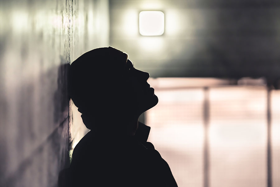 A sad man is silhouetted by the light while leaning in a hallway.