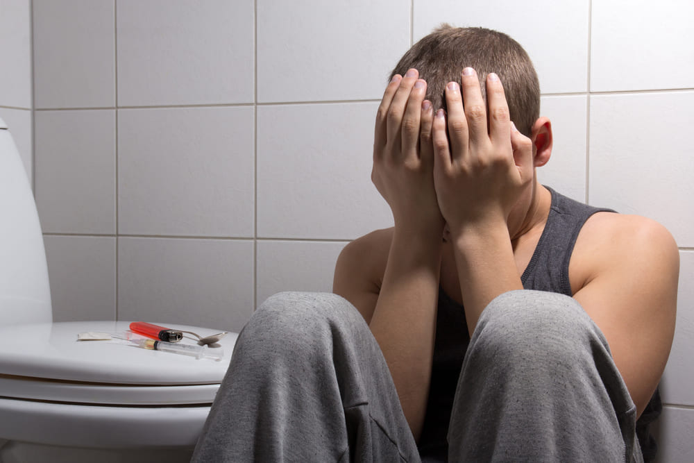 A stressed young person sitting next to drugs in the bathroom