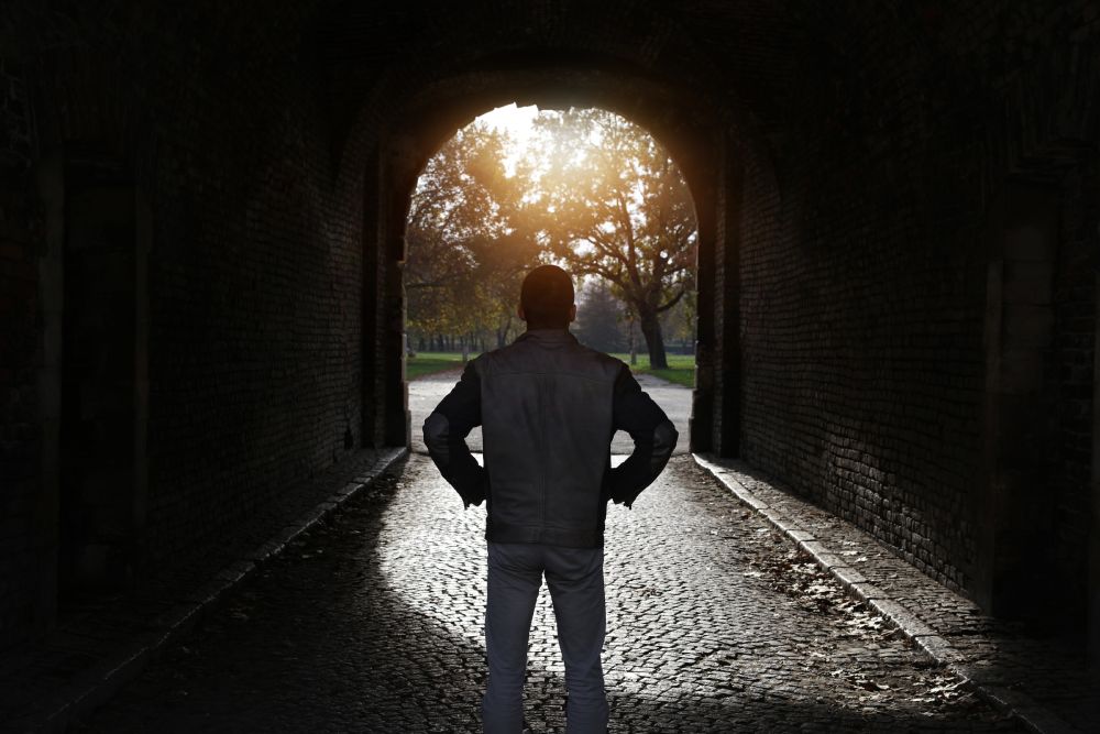 A person standing in a tunnel with a light at the end